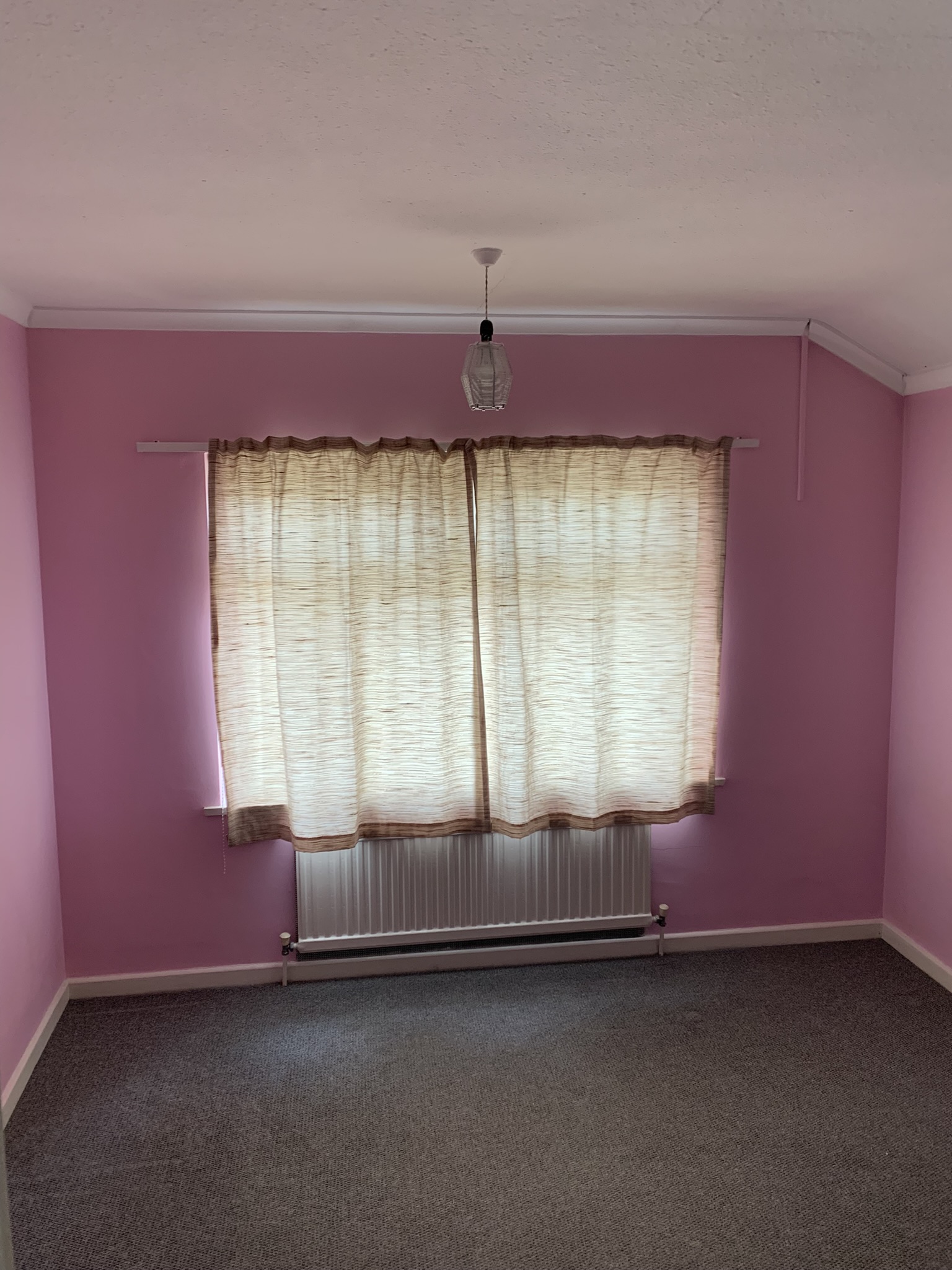 A view of a bedroom onto the window with pink wallpaper